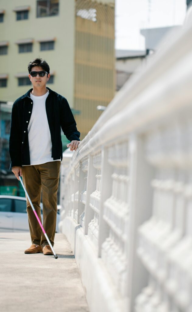 A visually impaired man walks confidently with a white cane on a city sidewalk.